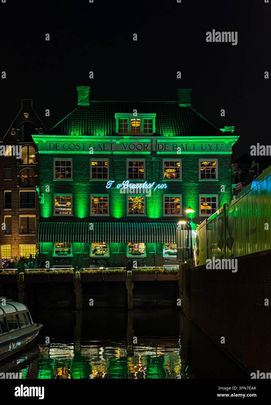 Historisches Ufergebäude in Grün beleuchtet bei Nacht entlang eines Kanals in Amsterdam, Niederlande. - Smartphone-aufgenommenes Stockfoto