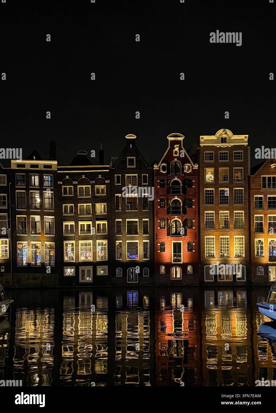 Traditionelle schmale Kanalhäuser bei Nacht beleuchtet mit Spiegelungen auf dem Wasser in Amsterdam, Niederlande. - Smartphone-aufgenommenes Stockfoto