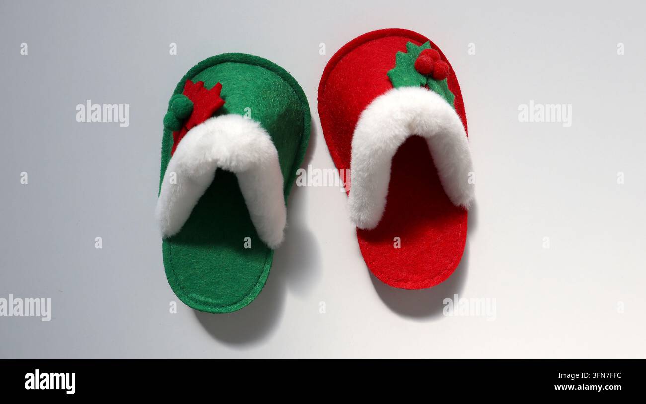 Ein Paar Pantoffeln liegt auf einer weißen Oberfläche. Ein Pantoffel ist grün mit weißer Bordüre und Verzierungen, der andere ist rot mit ähnlicher weißer Bordüre. Diese Stockfoto