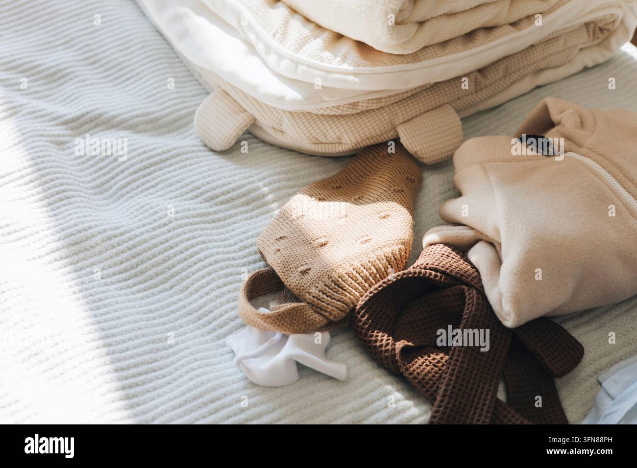 Neutrale Babykleidung und gestrickte Accessoires auf dem Bett Stockfoto