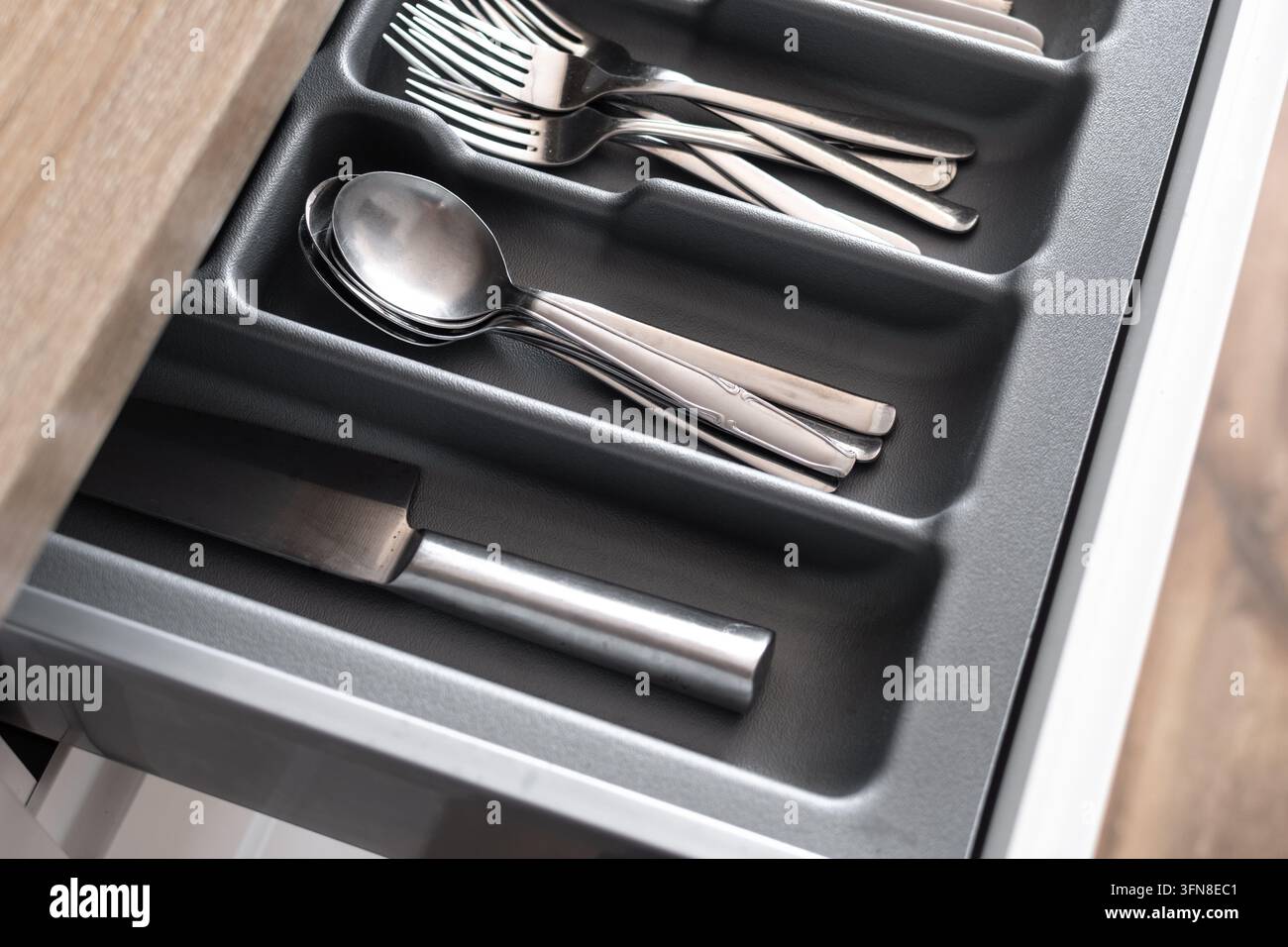 Nahaufnahme eines ordentlich angeordneten Besteckschubladens mit Löffeln, Gabeln, Messern und Küchenutensilien, die in einer dunklen Organiser-Schale in einer modernen Küchenausstattung verstaut sind Stockfoto