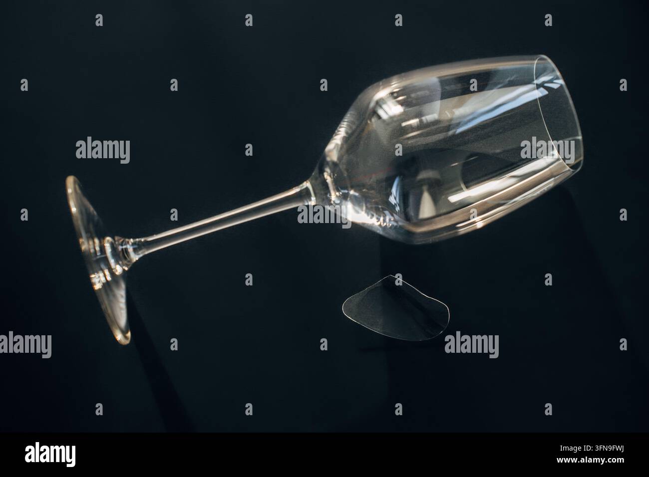 Zerbrochenes Weinglas mit abgetrenntem Glassplitter auf schwarzer reflektierender Oberfläche Stockfoto