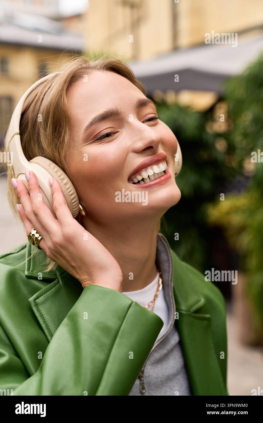 Eine junge Frau in stilvoller Freizeitkleidung lächelt, während sie draußen in der Stadt Musik hört. Stockfoto