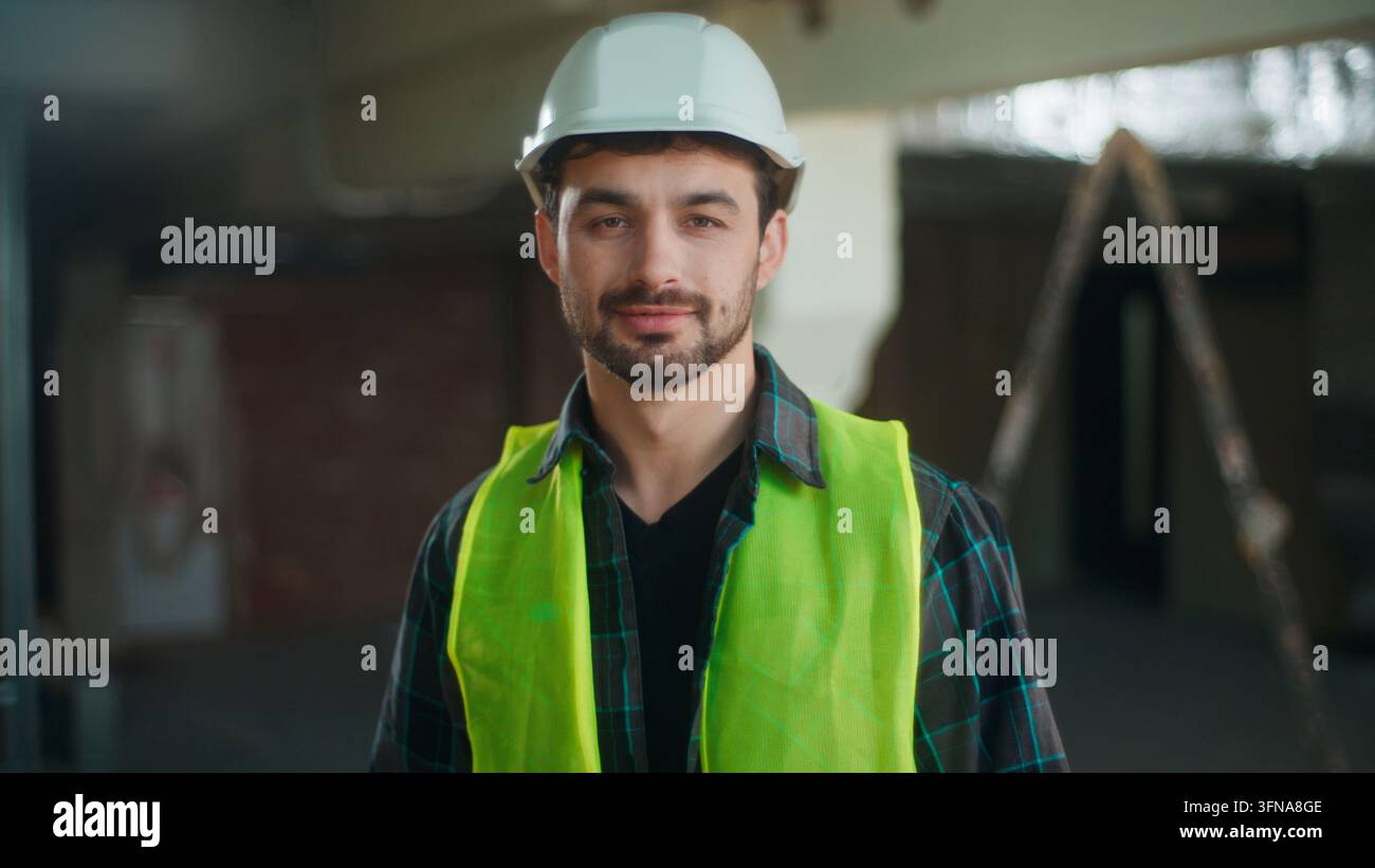 Fröhlicher kaukasischer Bauarbeiter lächelt in die Kamera, männlicher Bauunternehmer trägt Helm, Arbeiter posiert im Freien, selbstbewusster Bauleiter, Ingenieur, Vorarbeiter Stockfoto