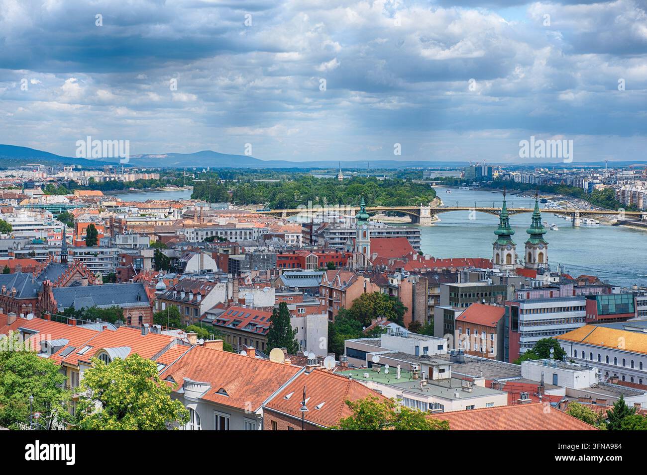 Ein weitläufiger Hochwinkelblick zeigt die Margaret-Insel in der Donau, flankiert von der lebendigen Stadtsilhouette von Budapest, Ungarn. Rotgedeckte Dächer und Stockfoto