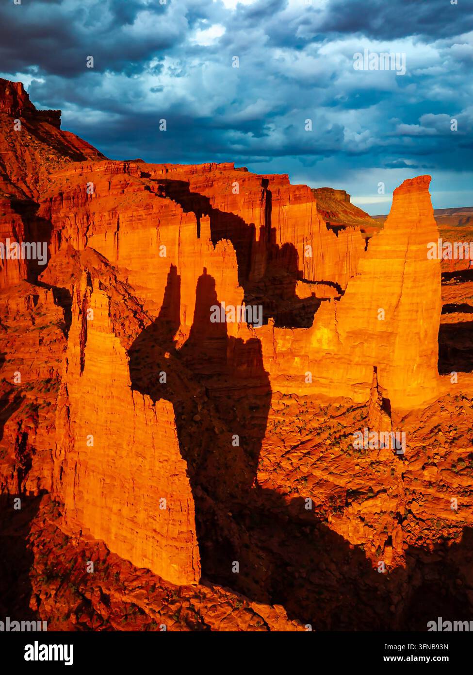 Lebendige Sonnenuntergangsfarben erleuchten aufragende Sandsteinspitzen und tiefe Wüstenschluchten unter dramatischen Himmeln bei Fisher Towers in der Nähe von Moab, Utah Stockfoto