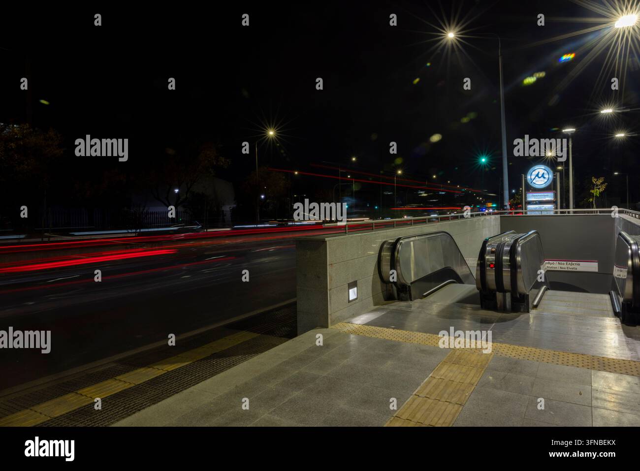 Thessaloniki, Griechenland – 28. November 2024: Der Eingang der Panepistimio-U-Bahn-Station ist nachts in Thessaloniki beleuchtet, mit Lichtspuren von Fahrzeugen Stockfoto