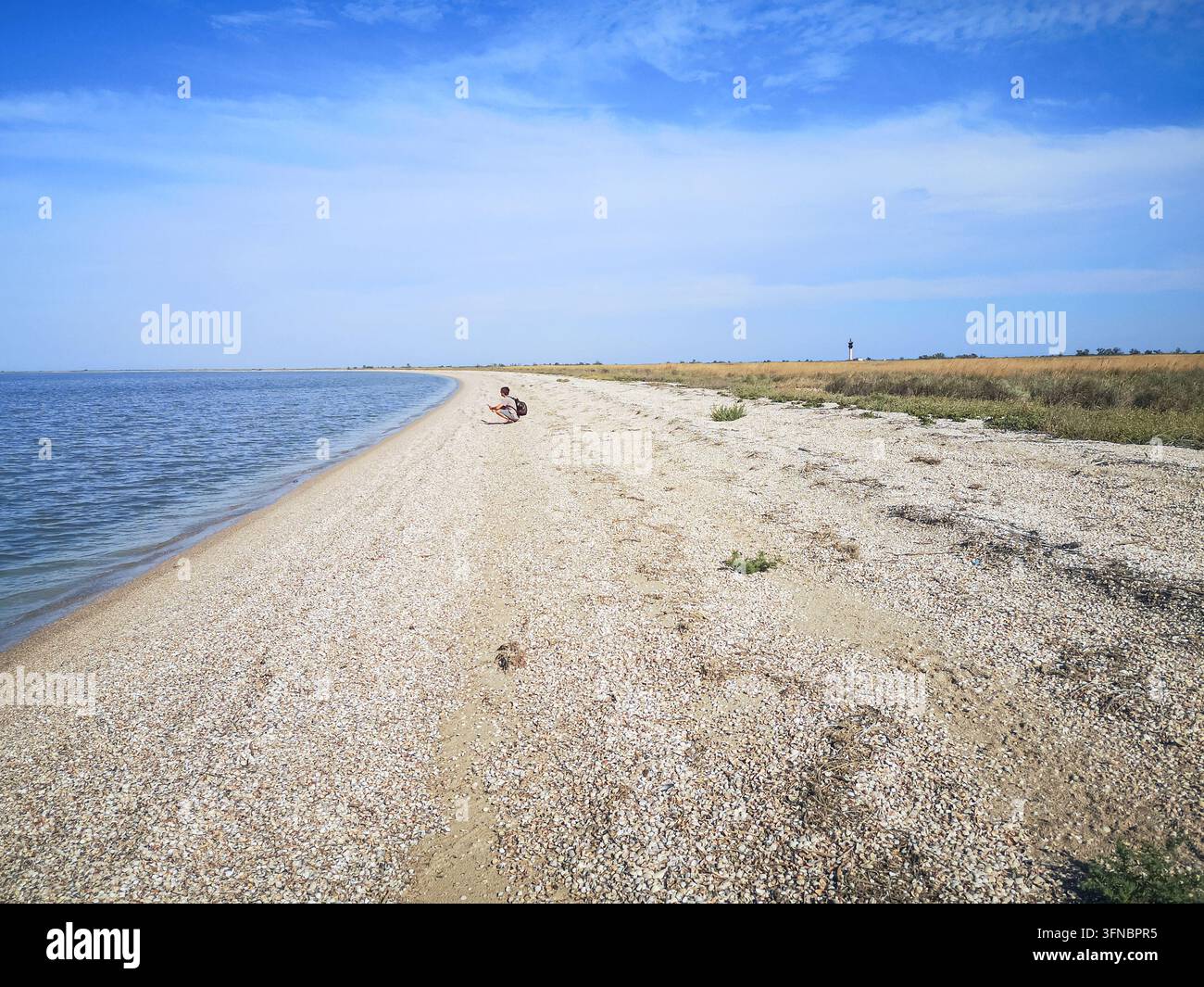 Männlicher Reisender auf sandigem Spieß der Shahany-Lagune mit dem Shahany-Leuchtturm in der Ferne im Nationalpark Tuzly-Lagunen, Oblast Odessa, Ukraine - Smartphone-aufgenommenes Stockfoto