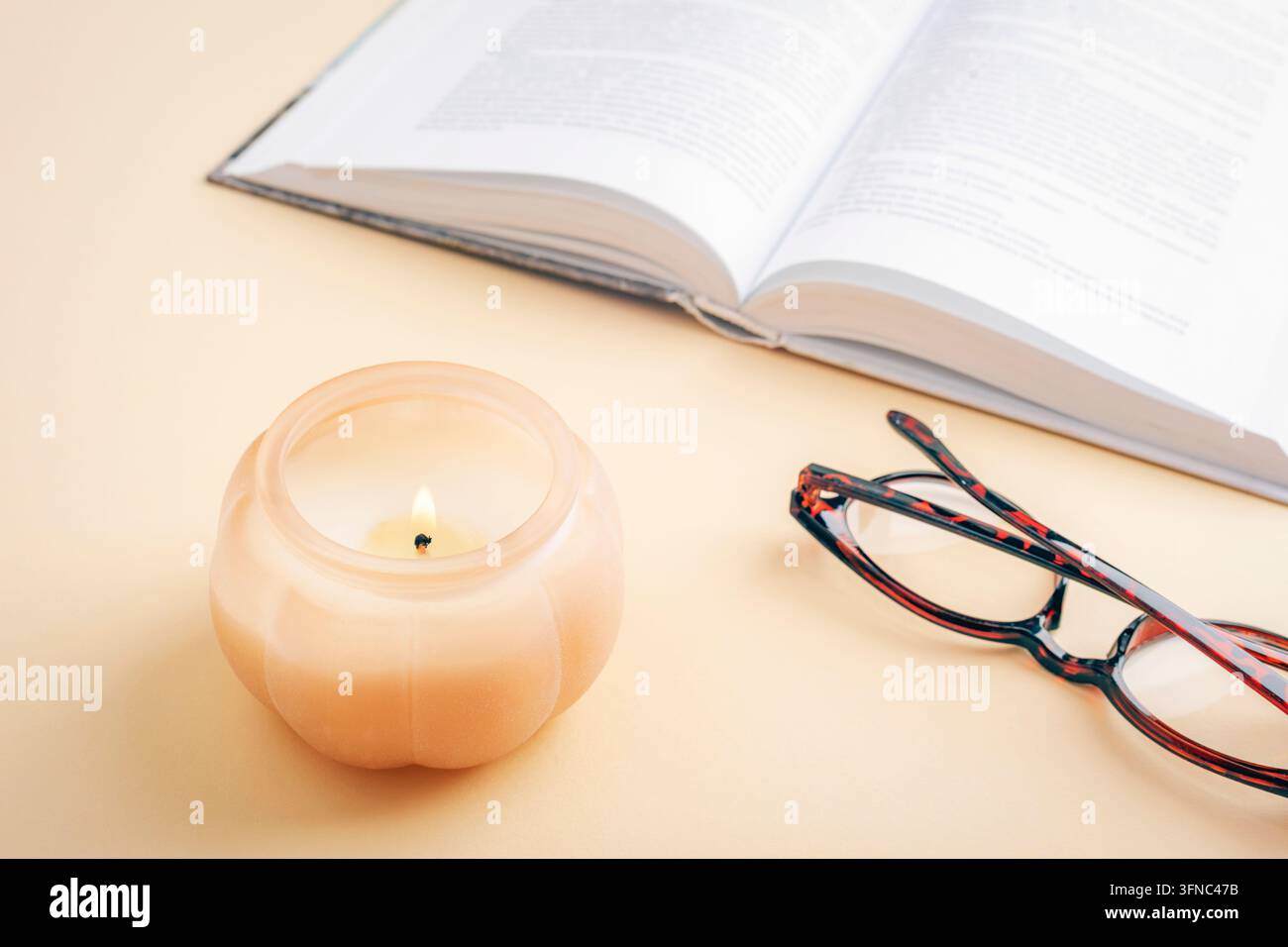 Duftkerze neben einem offenen Buch und einer Brille in einer warmen, gemütlichen Umgebung. Lesekonzept. Oberblick, Flat Lay. Stockfoto