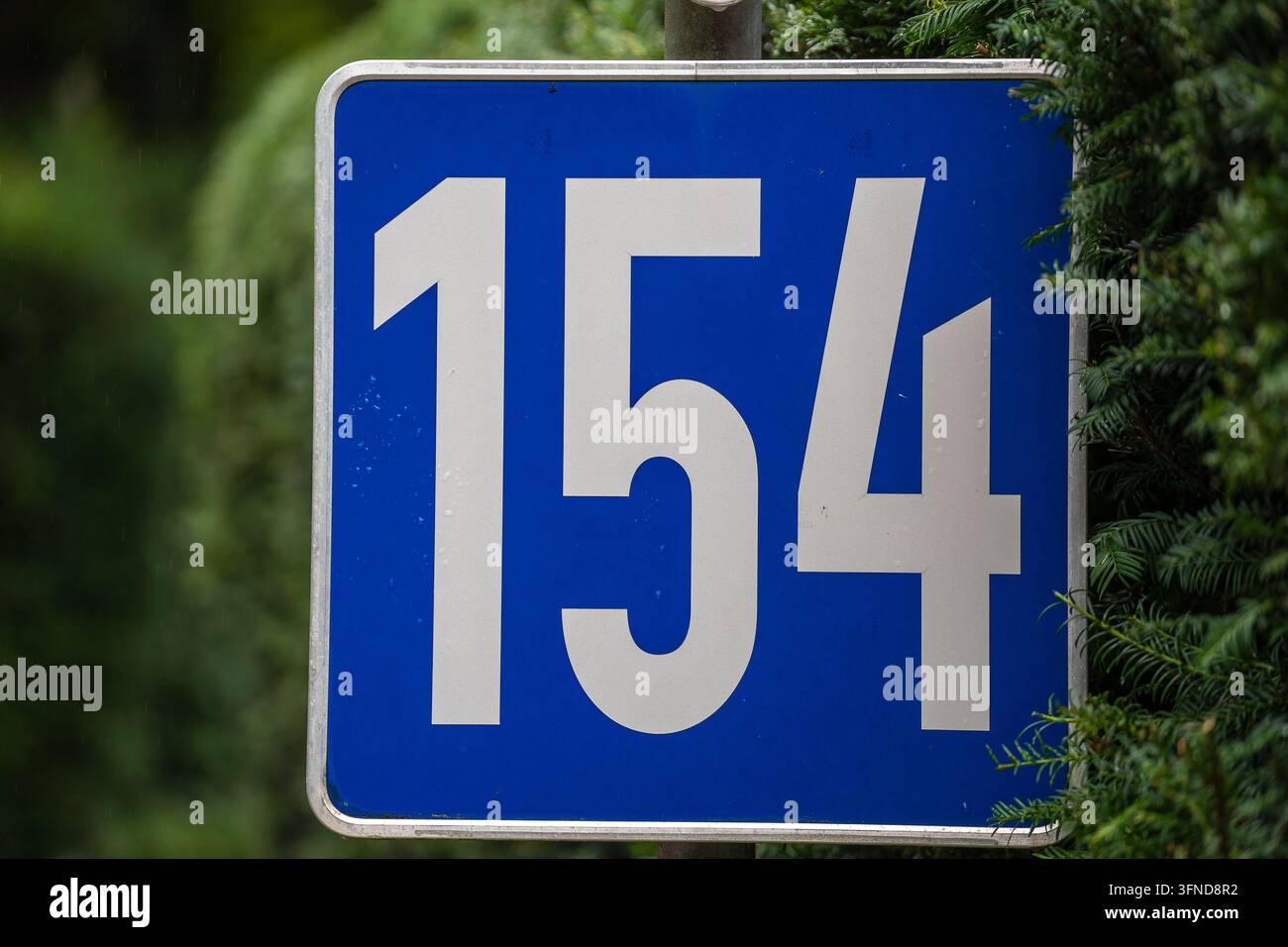 Ein blaues Hausnummernschild, das die Nummer einhundertvierundfünfzig, 154, auf der Straße in Österreich zeigt, Nahaufnahme Stockfoto