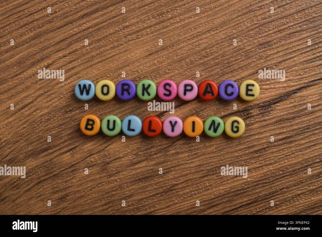 Bunte Buchstabenperlen, die Workspace Bullying auf einem Holz-Hintergrund buchstabieren, repräsentieren Mobbing am Arbeitsplatz, toxische Kultur, Mitarbeiterwohlbefinden, Respek Stockfoto