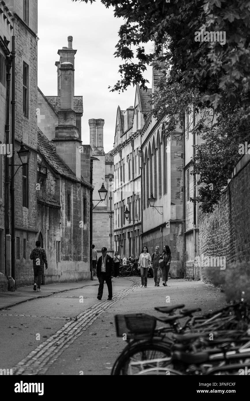 Schwarz-Weiß-Straßenszene auf der Brasenose Lane in Oxford, mit Menschen, die entlang der gepflasterten Gasse zwischen College-Gebäuden und geparkten Fahrrädern spazieren. Stockfoto