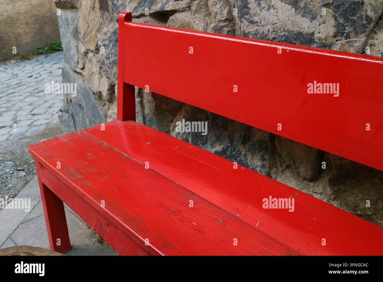 Nahaufnahme einer leeren rot gestrichenen Bank neben einer alten, felsenartigen Wand Stockfoto