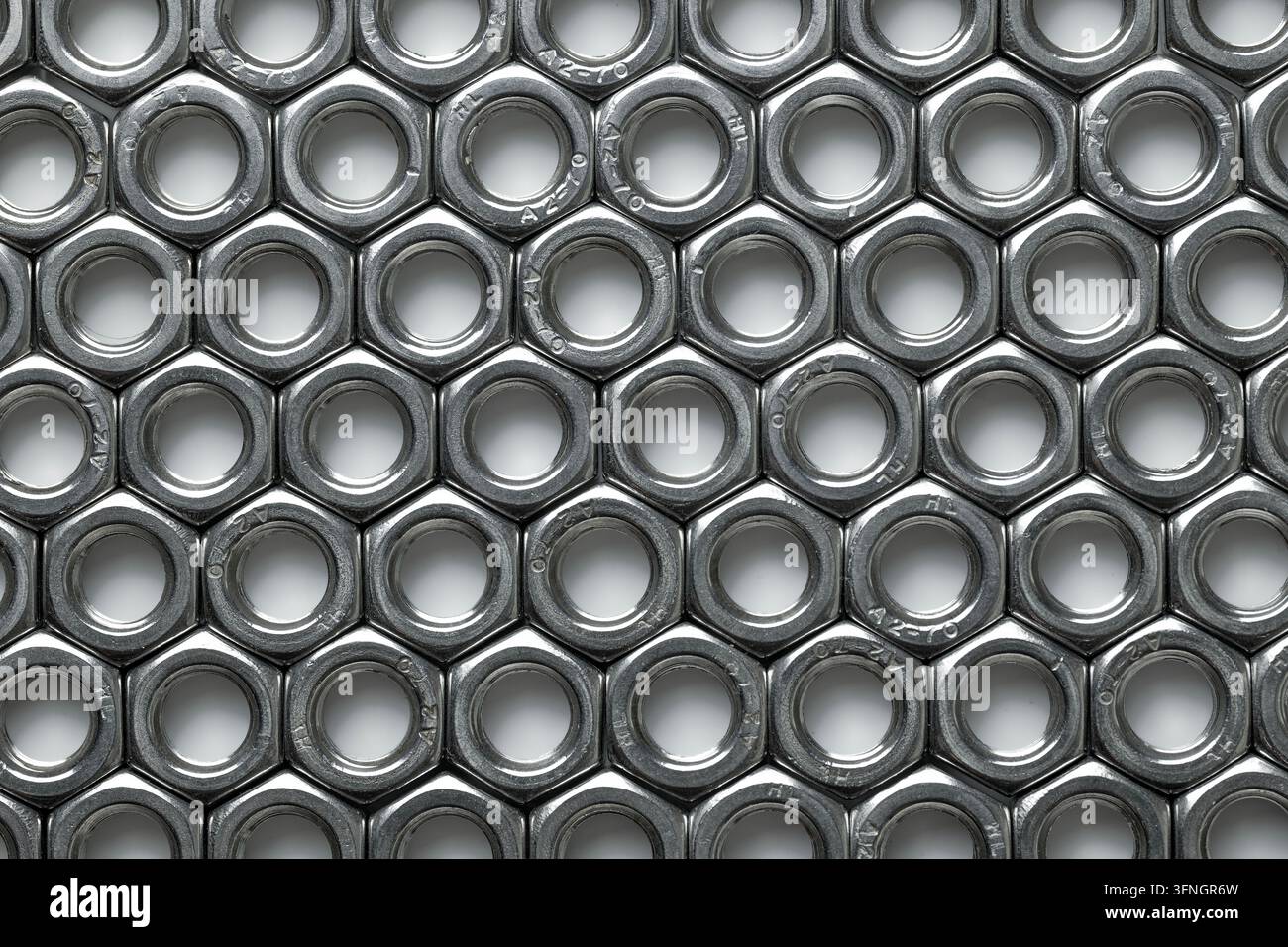 Metallnüsse, die ein sich wiederholendes Muster bilden, und Ingenieur- und Konstruktionselemente präsentieren Stockfoto
