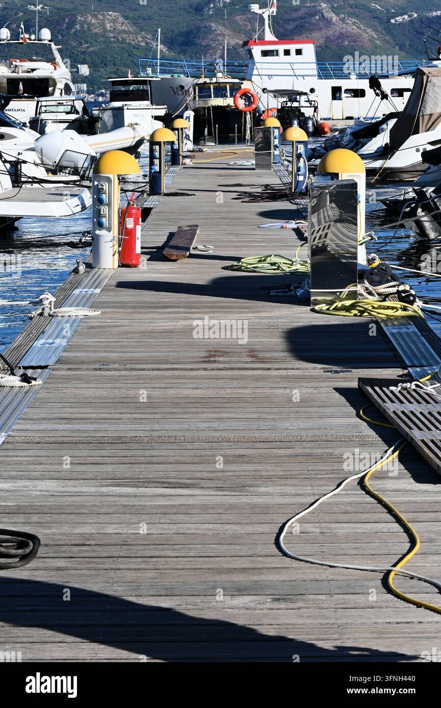 Vertikale detaillierte Makro-Stockfotografie, die einen hölzernen Marina-Pier mit Yachten, Sicherheitsausrüstung und Seilen im Freien bei natürlichem Tageslicht zeigt. Stockfoto