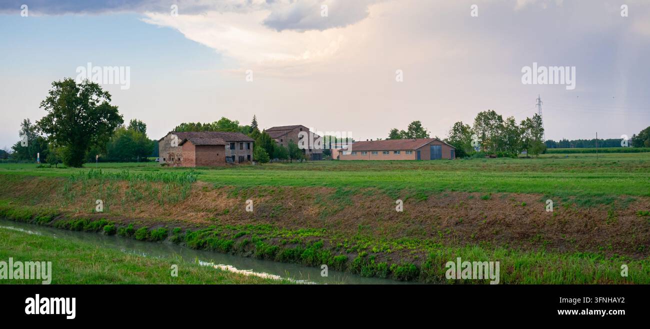 Friedliches ländliches Farmland mit Backstein-Bauernhäusern, grüne Felder in der Nähe eines kleinen Kanals im Poidelta, Norditalien. Stockfoto