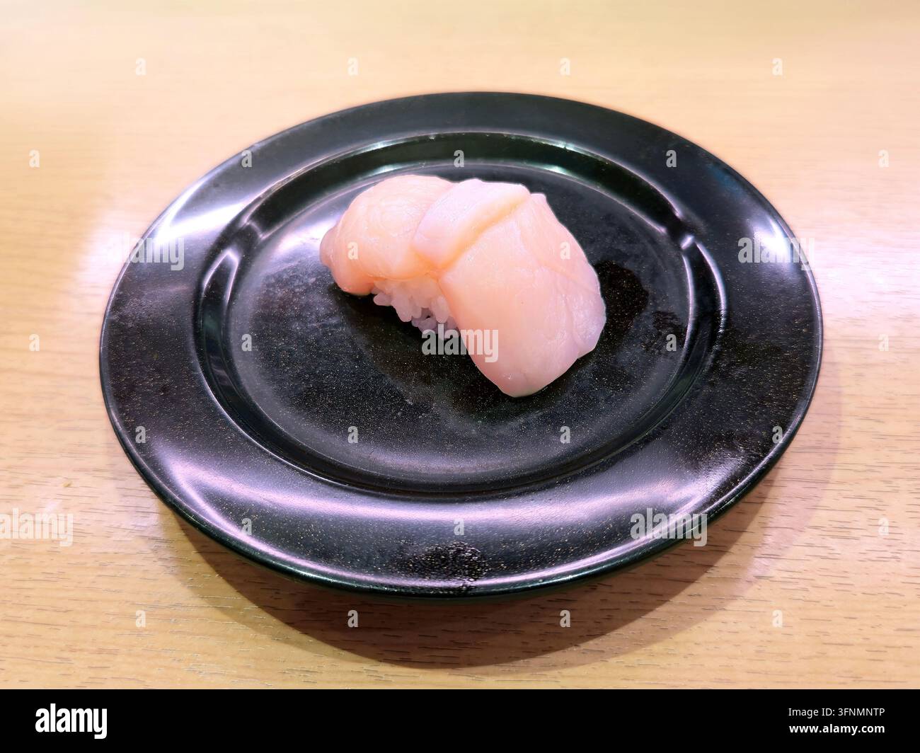 Frischer Scallop Nigiri Sushi mit rohen Scallopscheiben über gewürztem Reis, serviert auf einem schwarzen Teller in einem japanischen Restaurant. - Smartphone-aufgenommenes Stockfoto