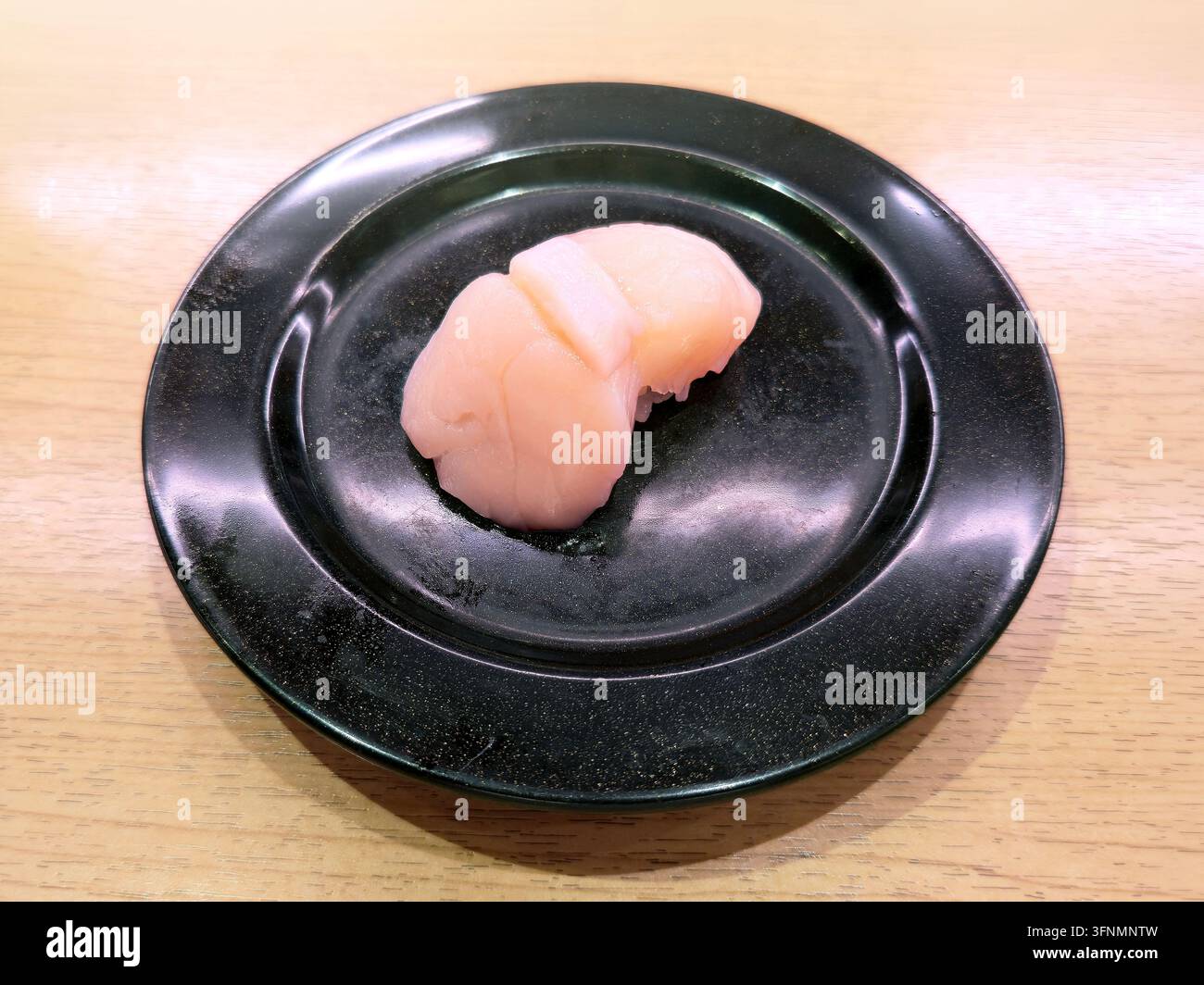 Frischer Scallop Nigiri Sushi mit rohen Scallopscheiben über gewürztem Reis, serviert auf einem schwarzen Teller in einem japanischen Restaurant. - Smartphone-aufgenommenes Stockfoto