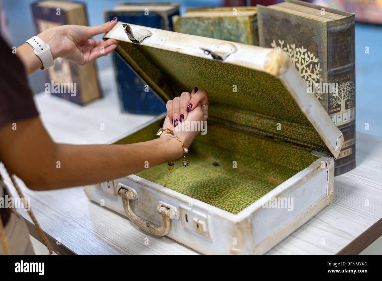 Frau öffnet einen Vintage-Koffer auf einem Tisch, umgeben von dekorativen Büchern, antiker Reisekoffer mit Retro-Interieur und nostalgischem Design. Stockfoto
