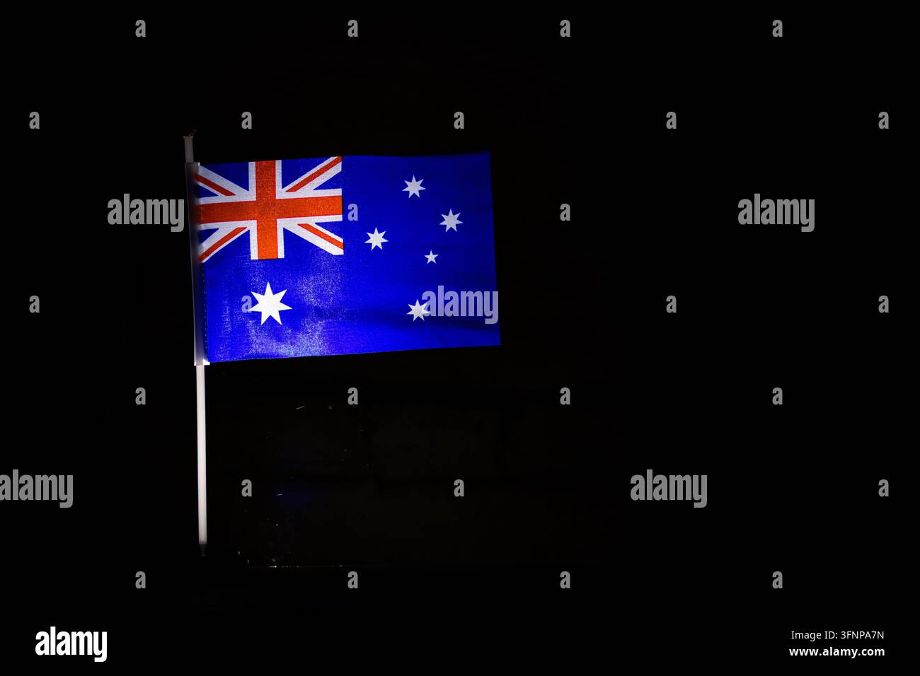 Australische Flagge leuchtet unter einem dunklen Himmel, während das Südkreuz und der Union Jack hell hervorstechen, der Stoff weht in einer stetigen Brise mit Platz für Text Stockfoto