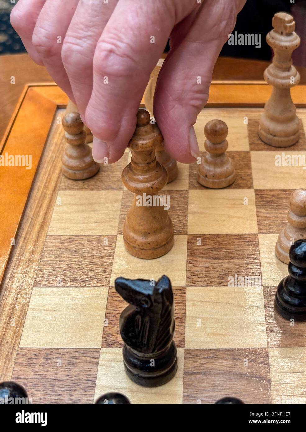 Schachbrett und Figuren mit der Hand einer älteren Person, die eine Schachfigur bewegt. Stockfoto