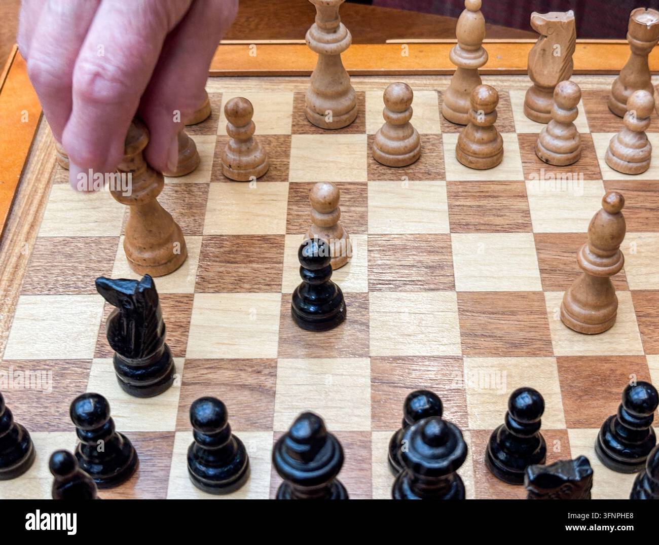 Schachbrett und Figuren mit der Hand einer älteren Person, die eine Schachfigur bewegt. Stockfoto