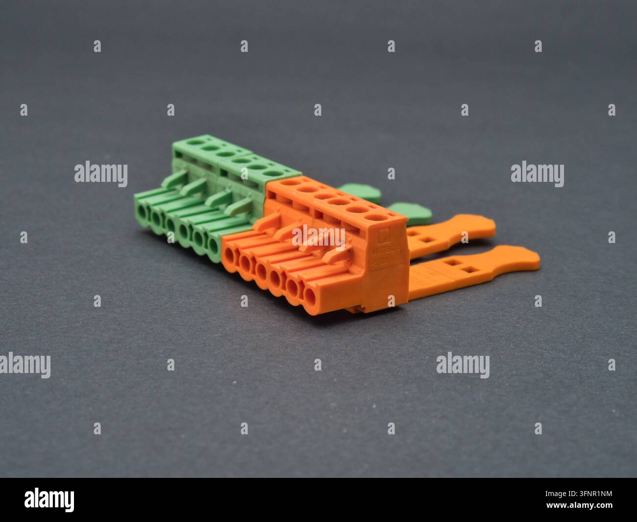 Bunte elektrische Klemmblöcke und - Eine Nahaufnahme von lebhaft grünen und orangefarbenen elektrischen Klemmblöcken mit Drahtverbindungswerkzeugen auf einem dunklen Hintergrund Stockfoto