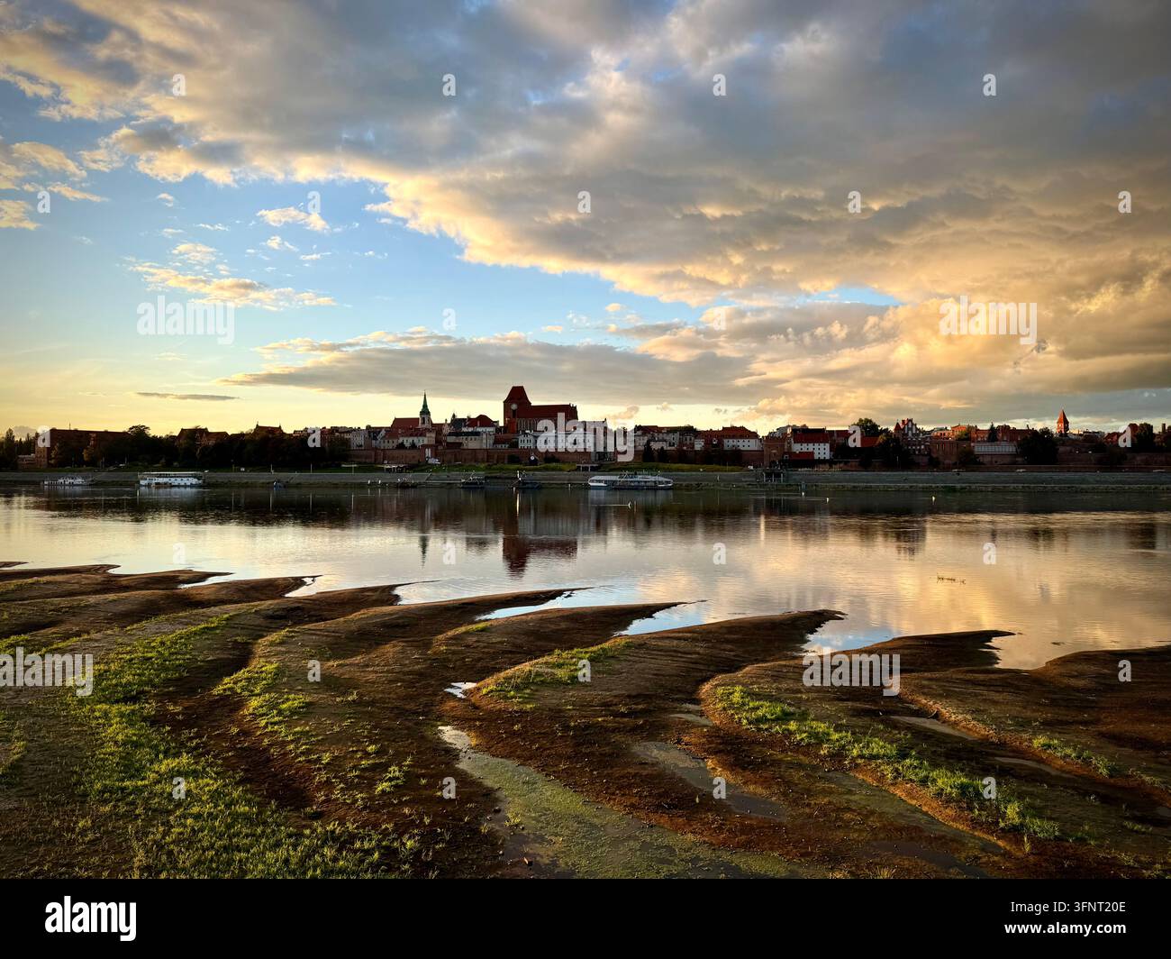 Breite horizontale Ansicht von Toruń, Polen, mit Skyline über der Weichsel, mittelalterlichen Backsteingotikkathedralen und goldenen Wolkenreflexionen - Smartphone-aufgenommenes Stockfoto