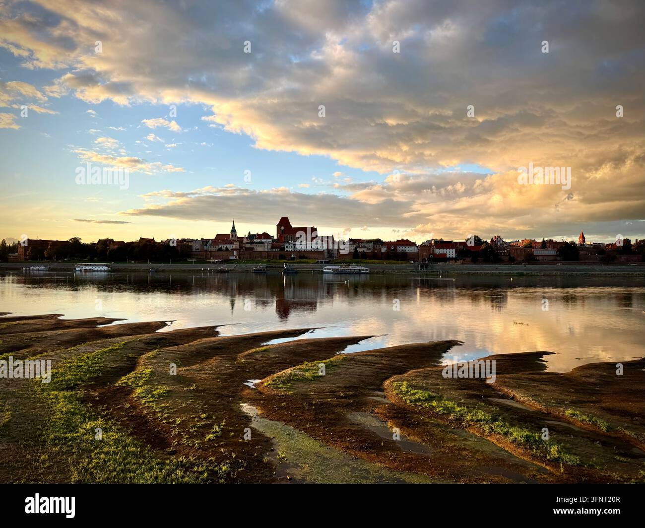 Breite horizontale Ansicht von Toruń, Polen, mit Skyline über der Weichsel, mittelalterlichen Backsteingotikkathedralen und goldenen Wolkenreflexionen - Smartphone-aufgenommenes Stockfoto