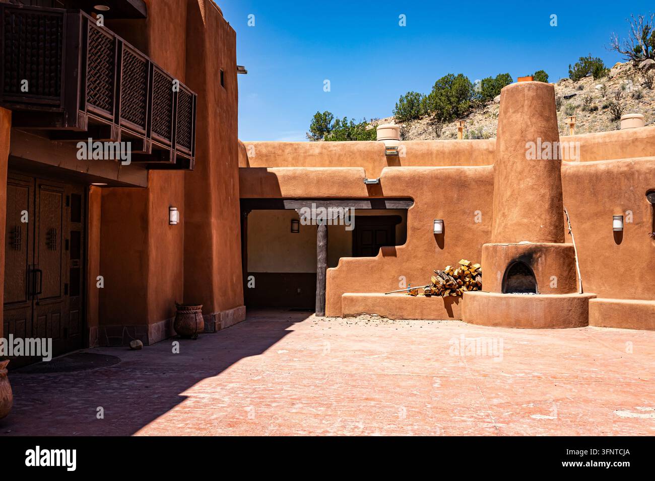 Abiquiu, New Mexico, USA, 24. Mai 2024: Landschaftsansicht eines Terrakotta-Adobe-Hofes, runder Außenkamin, verglaster Balkon und geschnitzte Türen. GP Stockfoto