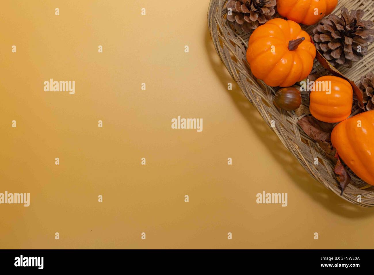 Kleine Kürbisse und Herbstelemente, die in einem Weidenkorb auf einem goldenen Hintergrund arrangiert sind Stockfoto