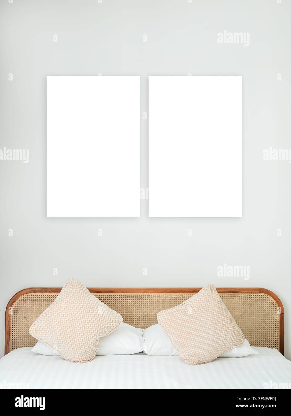 Zwei leere vertikale weiße Rahmen an einer weichen grauen Wand über einem Bett mit Kissen und gewebtem Rattan-Kopfteil, ideal für Postermockups, Wandkunstpräsentationen Stockfoto