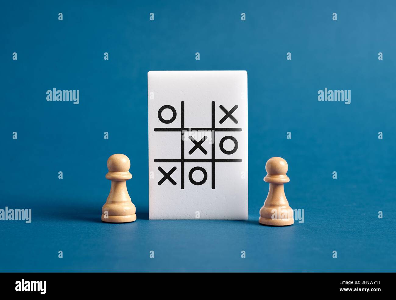 Zwei Schachbauern stehen gegenüber einem Tic-Tac-Toe-Spiel und symbolisieren Geschäftsstrategie, Wettbewerb und Entscheidungsfindung Stockfoto