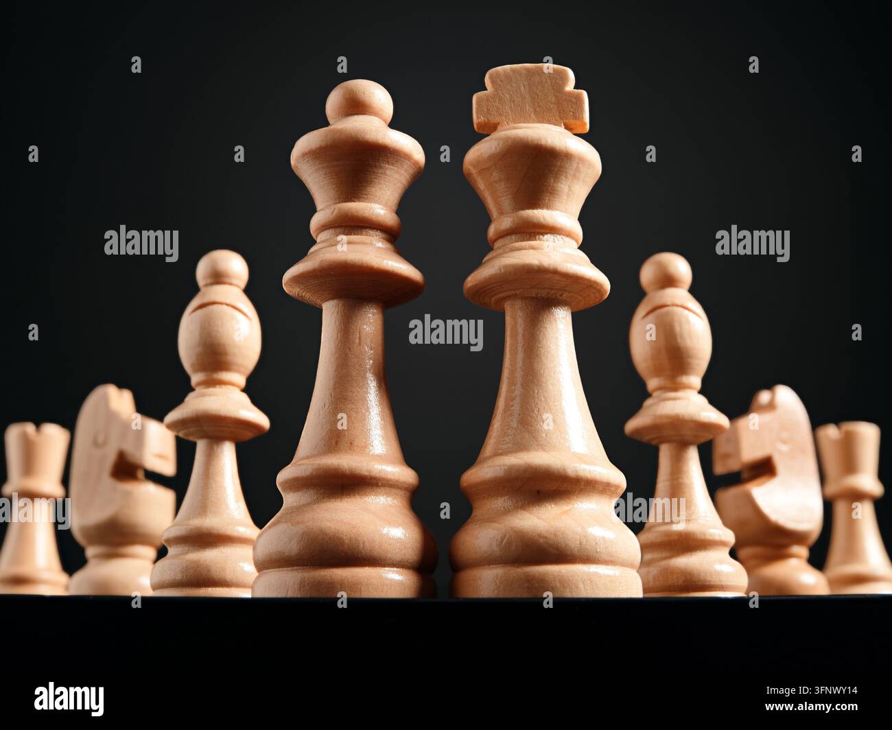 Holzschachfiguren mit König und Dame in der Mitte vor dunklem Hintergrund. Strategische Führung, Teamarbeit, Partnerschaft, Unternehmensführung und Macht Stockfoto