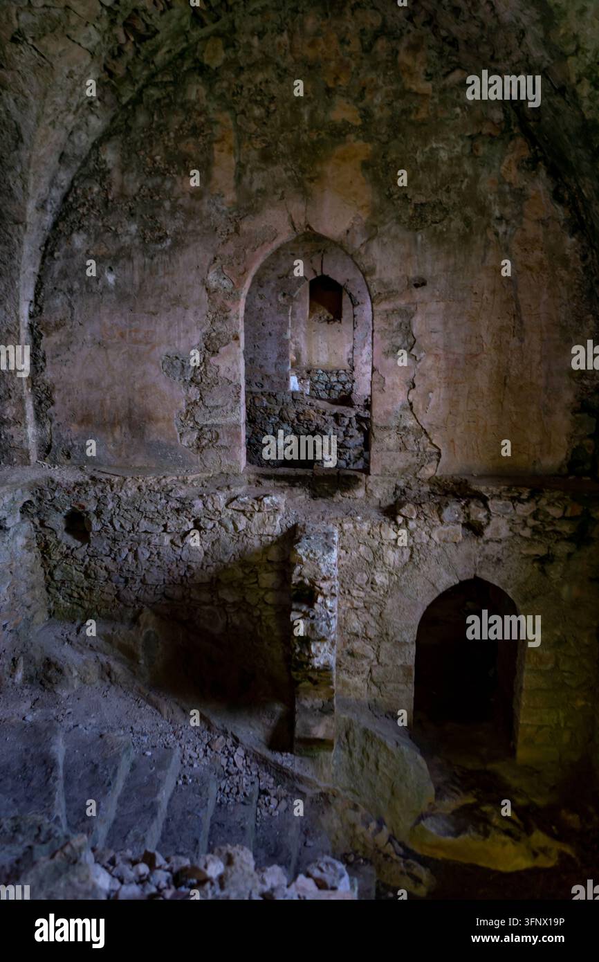 Dunkles verlassenes Steininnere mit gewölbten Türöffnungen, bröckelnden Wänden, Schutt und alter Mauerarbeit in einer antiken unterirdischen Ruine. Stockfoto