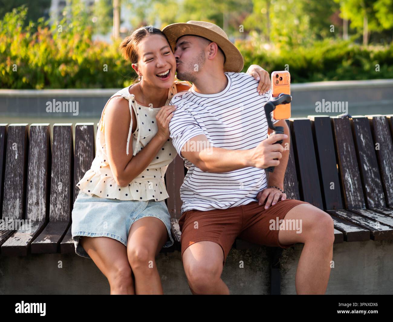 Lifestyle-Inhalts-Ersteller nehmen einen lustigen Moment zusammen auf einer Parkbank im warmen Sonnenlicht auf. Stockfoto
