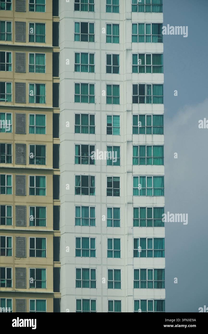 Moderne Hochhaus-Wohnungsgebäudefassade mit grün getönten Fenstern und kontrastierenden Wandfarben vor einem blauen bewölkten Himmel Stockfoto