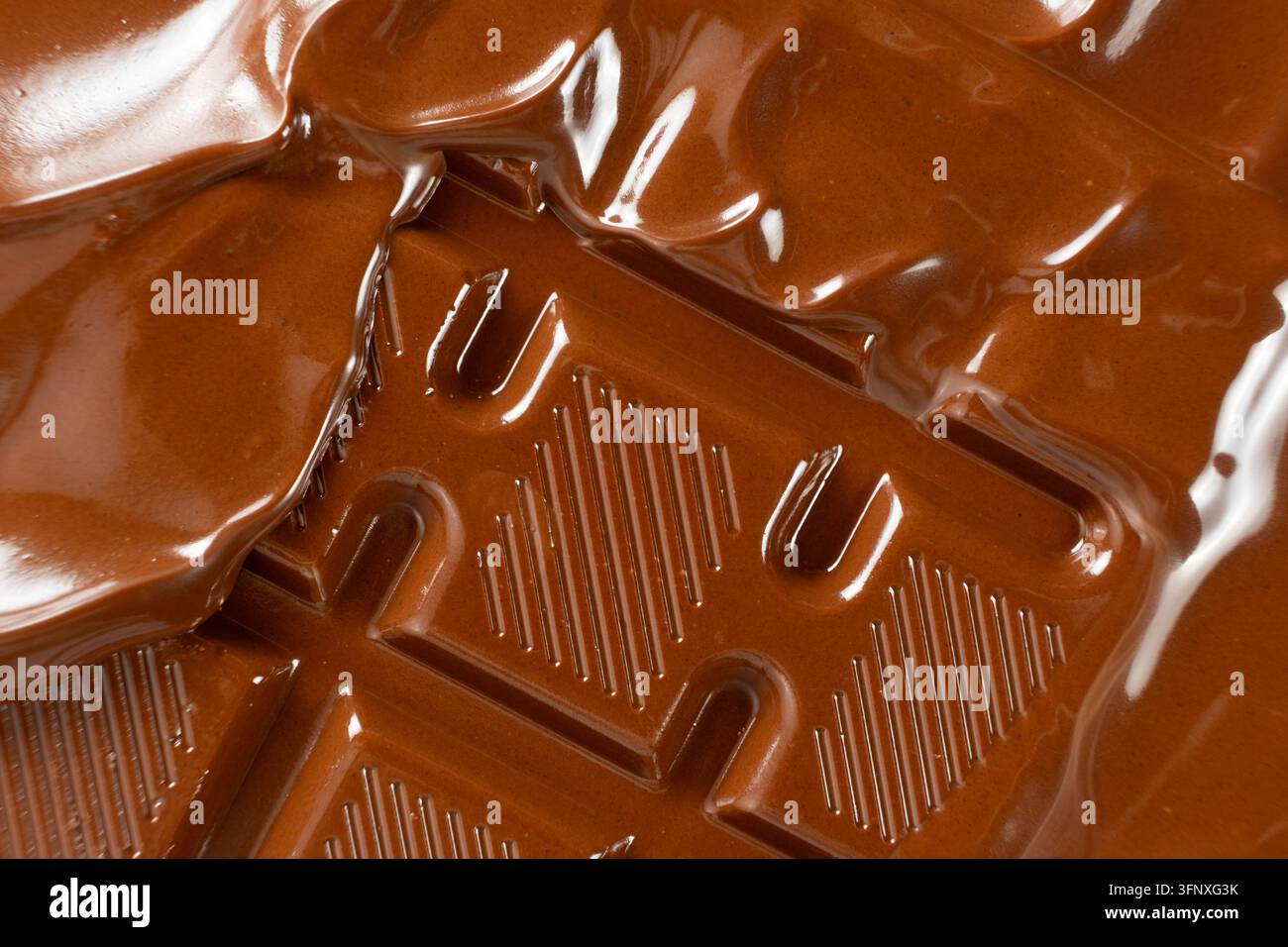 Warme flüssige Schokolade, die über eine feste Milchschokoladenriege fließt, Makroaufnahme Stockfoto