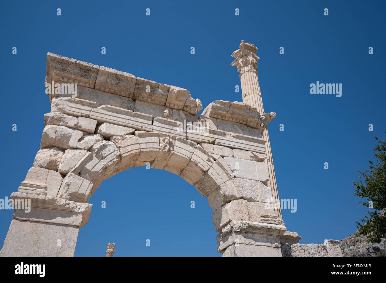 Dekorative Bänder umspannen die breite Öffnung, mit einem kleineren gebrochenen Schaft vor der höheren Säule. Oberflächenabnutzung und abgebrochene Kanten heben sich gegen Stockfoto