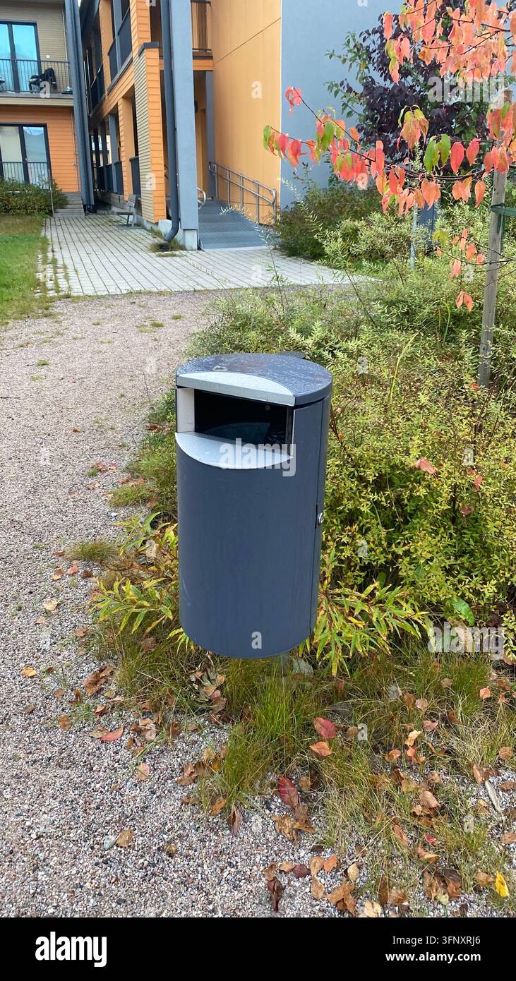 Outdoor-Mülltonne neben einem Wohnapartmenthaus, umgeben von Herbstvegetation Stockfoto