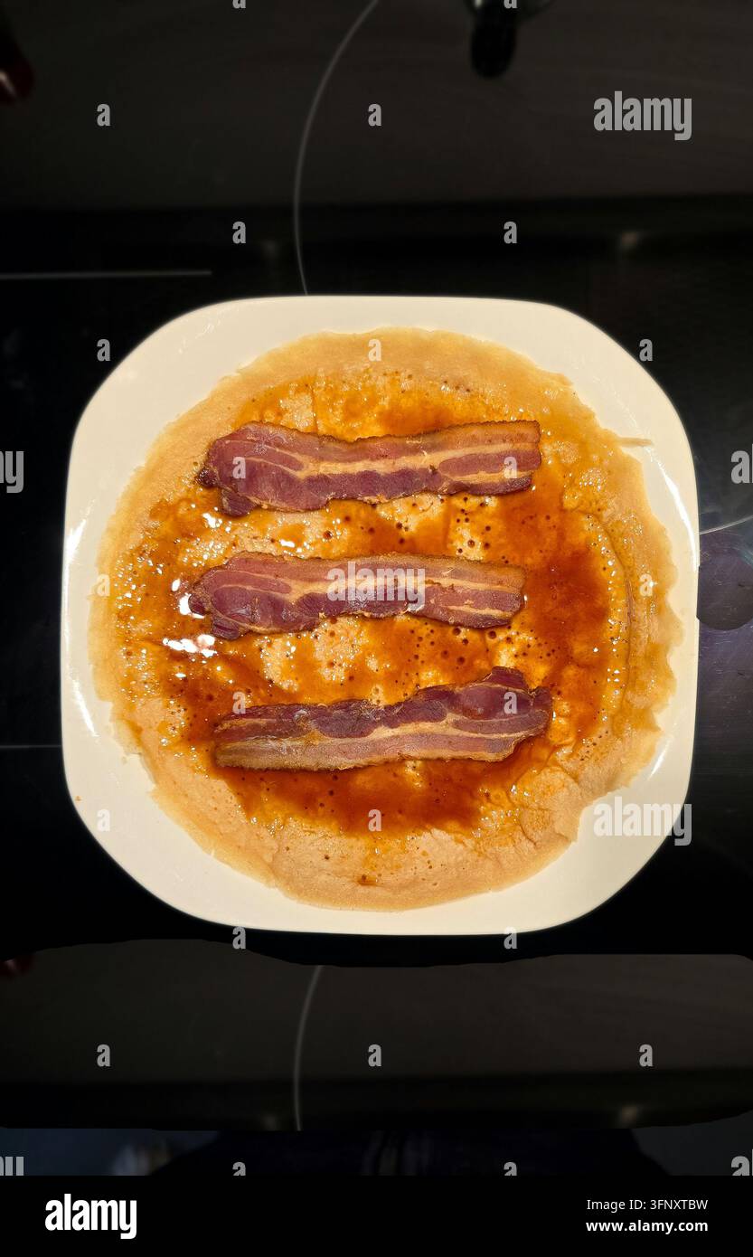 Pfannkuchen mit Sirup und drei knusprigen Streifen Speck auf einem weißen Teller Stockfoto
