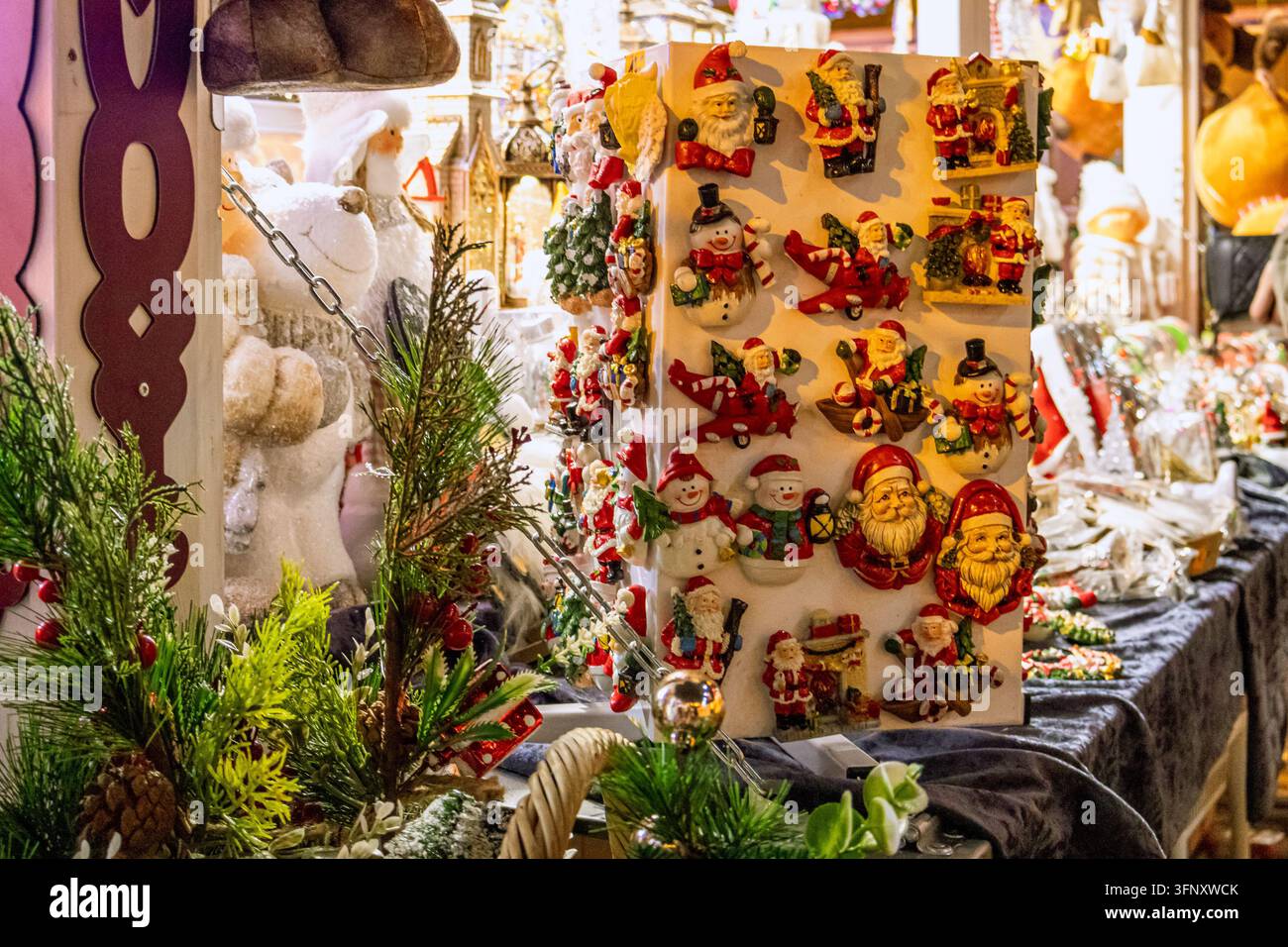 Drehständchen mit handgemachten Weihnachtsmann- und Schneemann-Magneten zwischen Tannenzweigen und Plüschtieren an einem Souvenirstand auf einem Weihnachtsmarkt. Konzept des Festes Stockfoto