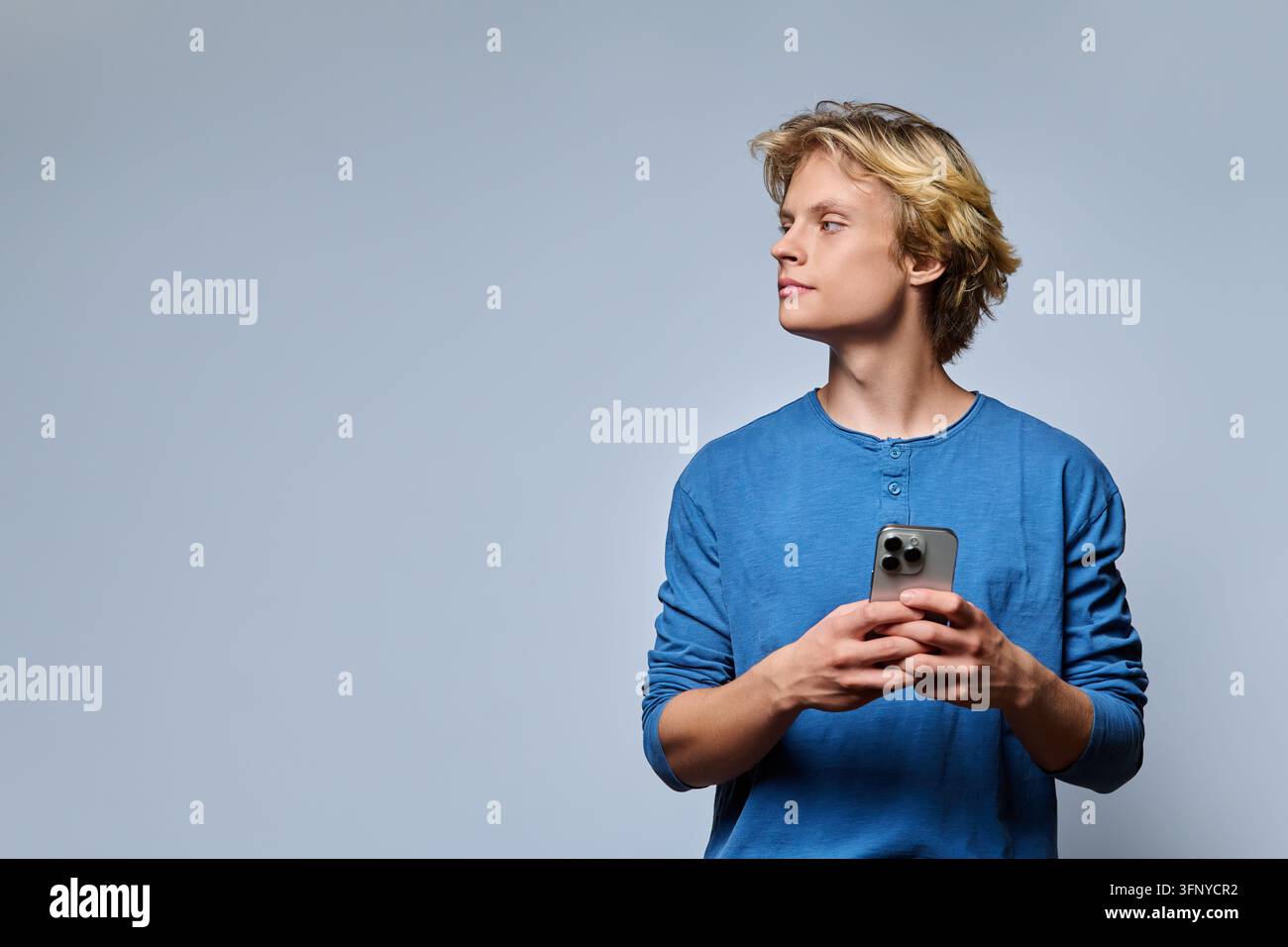 Junger Mann hält ein Smartphone und schaut weg im Studio-Porträt Stockfoto