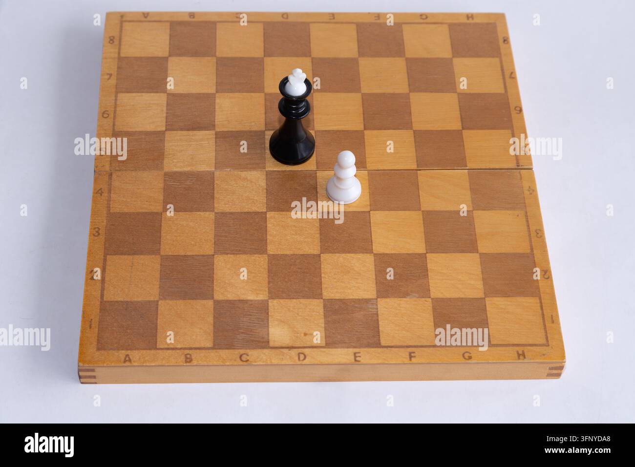 Schwarzer Schachkönig mit weißem Bauern oben steht einem einzelnen weißen Bauern auf einem leeren Holzbrett gegenüber. Stockfoto