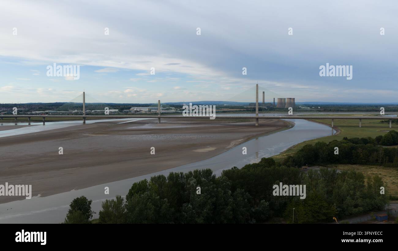 Luftaufnahme der Mersey Gateway Bridge, die den Fluss Mersey überspannt, mit Schlickflächen, Industriegebäuden und grünen Bäumen unter einem bewölkten Himmel in Runcor Stockfoto