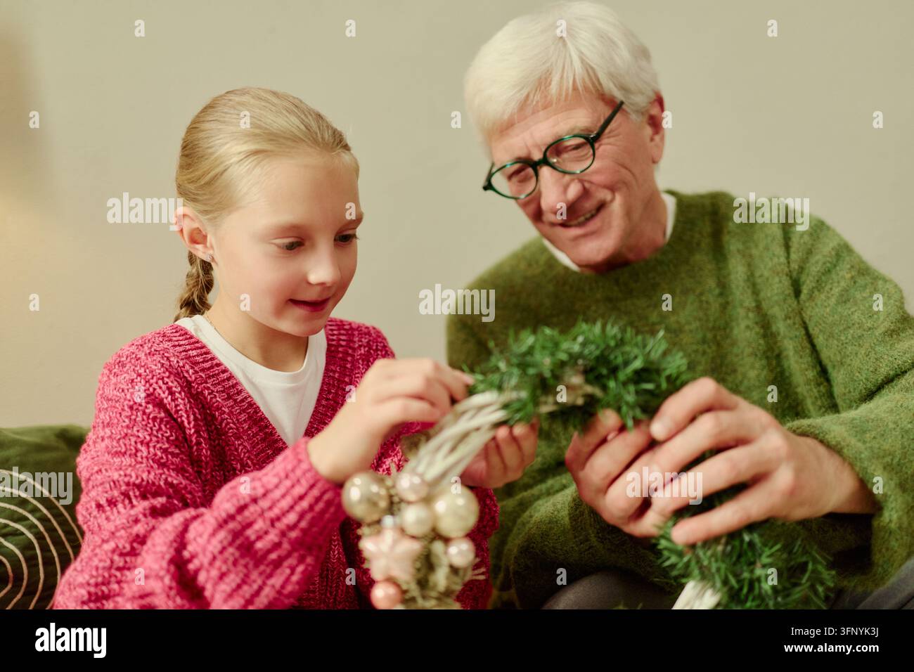 Senior Mann und Mädchen schmücken einen Weihnachtskranz zu Hause Stockfoto