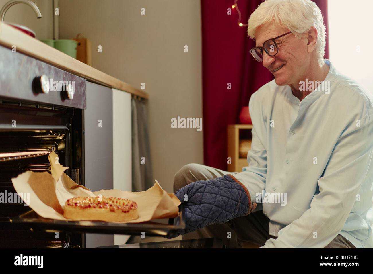 Senior Mann holt frisch gebackenen Beerenkuchen aus dem Ofen Stockfoto