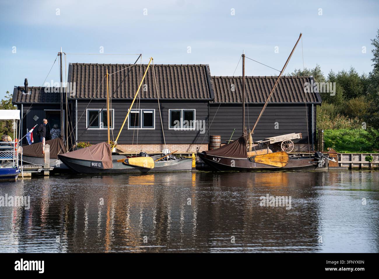 Kinderdijk, Niederlande - 2. OKTOBER 2026: Traditionelle Holzschuppen mit festgemachten Segelbooten und Besuchern auf dem Kanal in Kinderdijk Stockfoto