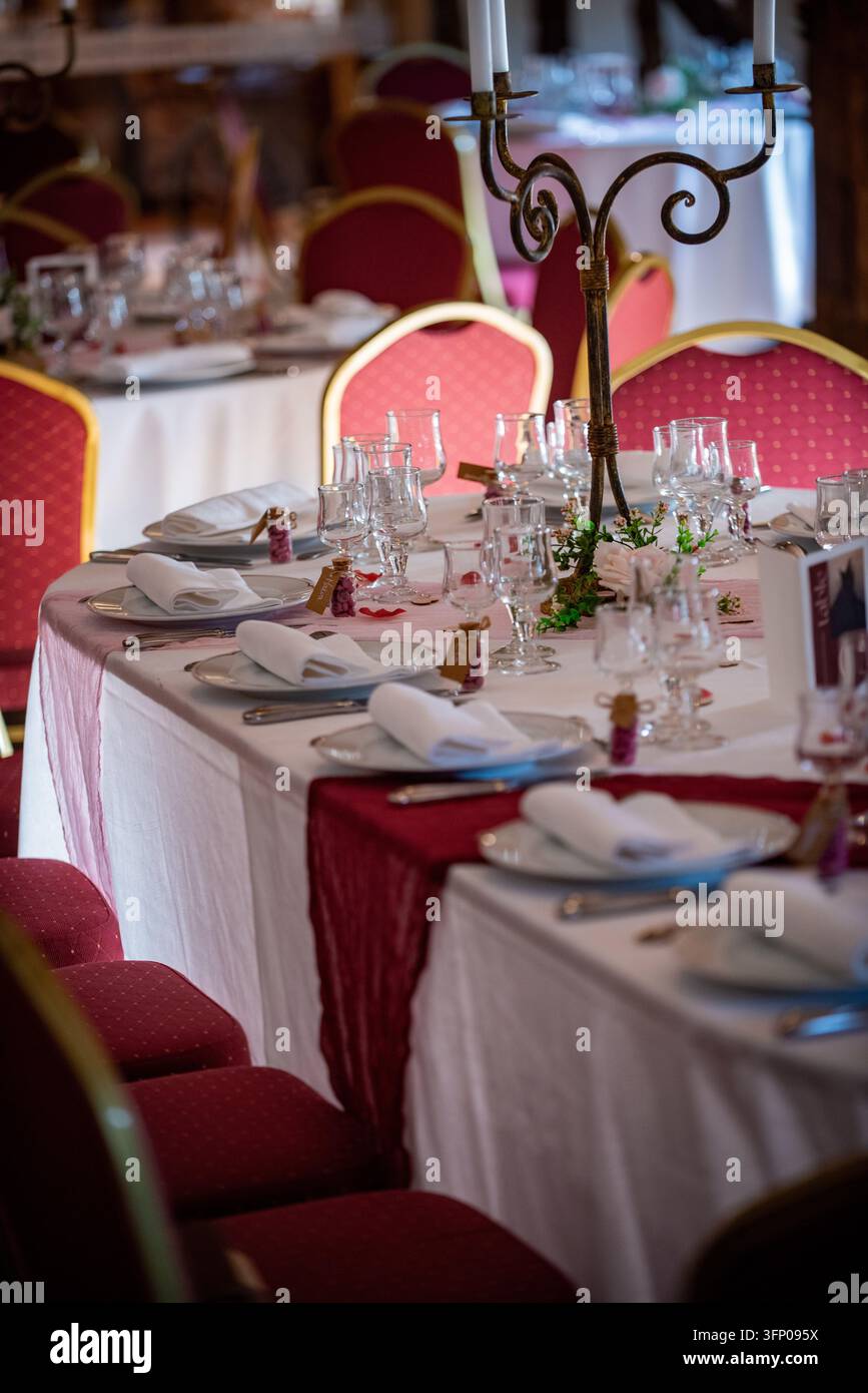 Nahaufnahme eines Hochzeitstisches mit Stielgläsern, gefalteten Servietten, weißen Tellern und kleinen Glasfläschchen gefüllt mit rosa Süßigkeiten-Geschenken, mit Rosenblättern Stockfoto
