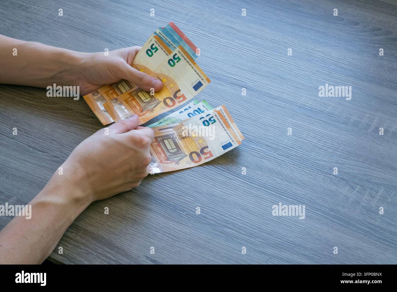 Hände, die Euro-Banknoten halten und sortieren, einschließlich Fünfzig-, Zwanzig- und Zehn-Euro-Noten auf einer grauen Holzoberfläche, von oben betrachtet Stockfoto